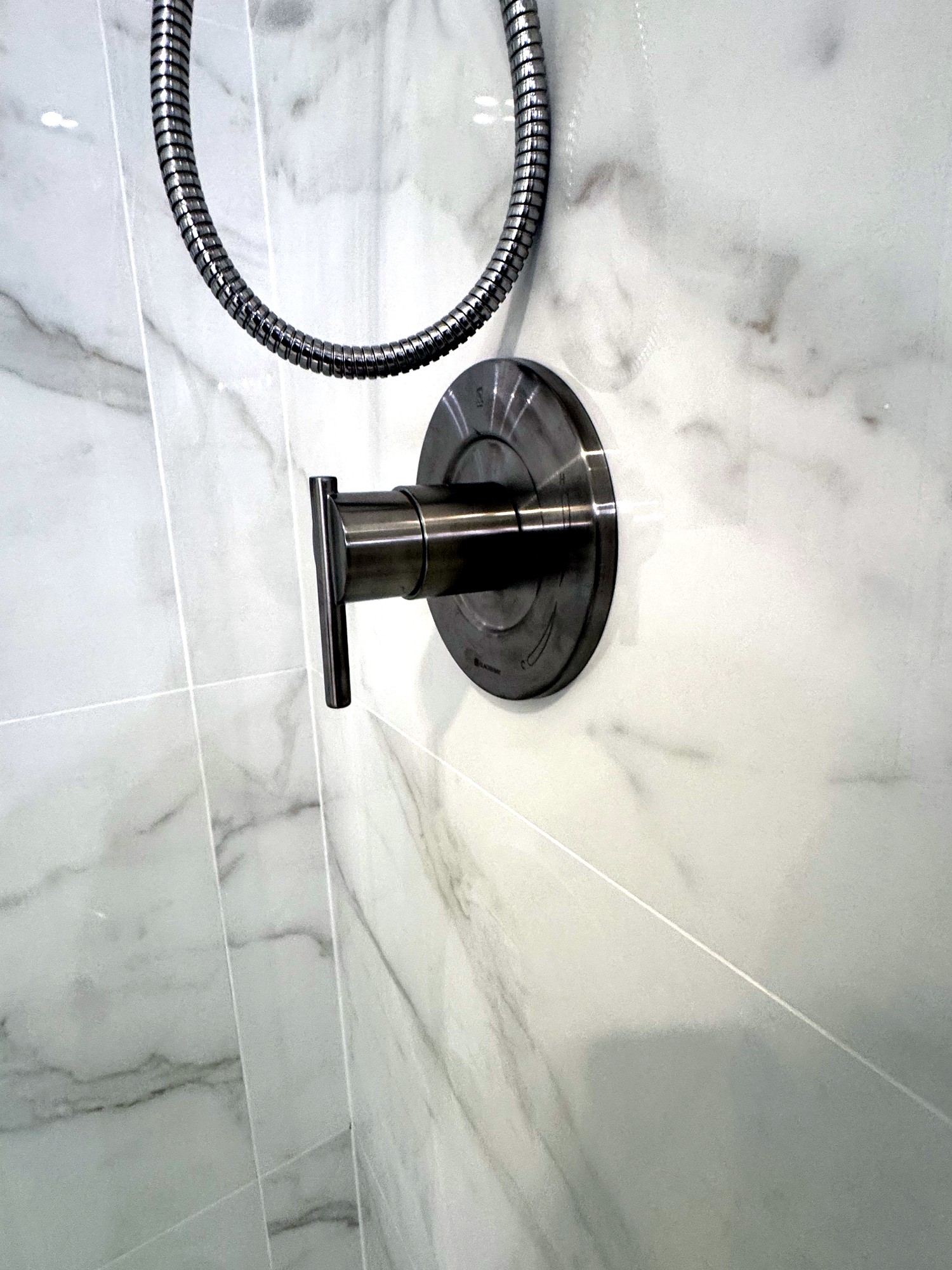Detail shot of brushed nickel shower valve and handheld sprayer on marble tile